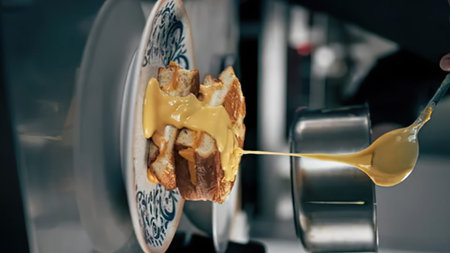 A close-up shot of cheese sauce being poured over a dish on a decorative plate.
