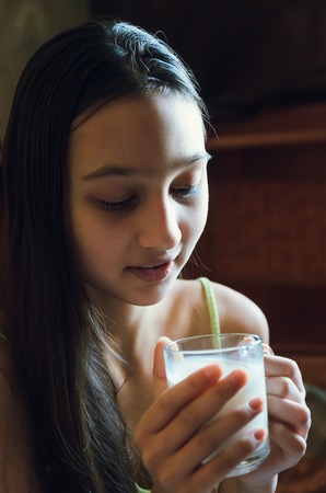 Pretty young brunette enjoying a glass of milk at home and smilingの写真素材