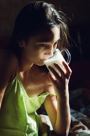 Pretty young brunette enjoying a glass of milk at home and smilingの写真素材