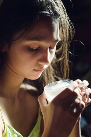 Pretty young brunette enjoying a glass of milk at home and smilingの写真素材
