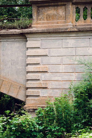 Fragment of a beautiful old stone wall with an arch in a thicket of grass.