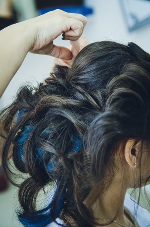 Closeup of a professional hairdresser's hands doing a hairstyle in a beauty salon. Model brunette, in the hair some of the strands are painted blue. The concept of fashionable stylish hairstyle, professional work with hair.の写真素材