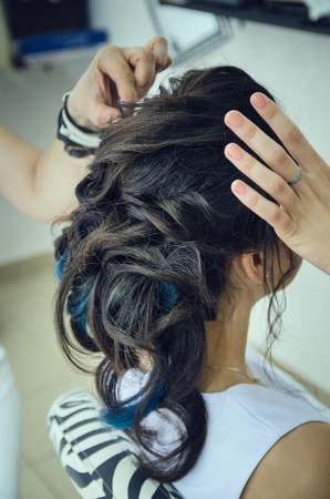 Closeup of a professional hairdresser's hands doing a hairstyle in a beauty salon. Model of a brunette with long hair. The concept of fashionable stylish hairstyle, professional work with hair.の写真素材