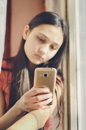 Beautiful teen girl holding a mobile phone. Lifestyle style.の写真素材
