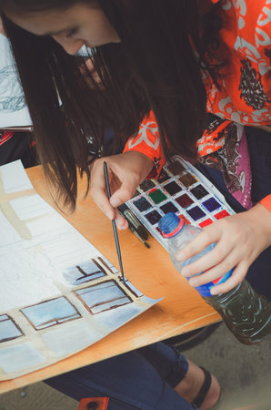 A teenager girl paints a picture with watercolors.