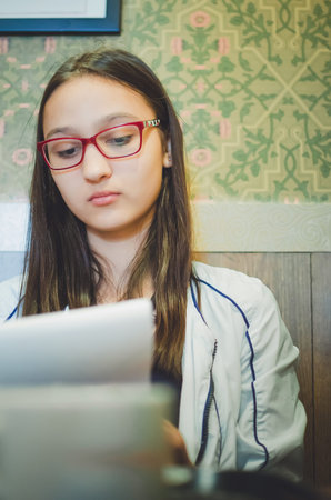 Cute girl student with glasses makes entries in the bloknot.