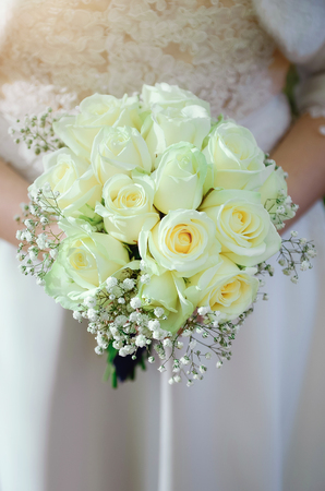 A bride in a white wedding dress is holding a bouquet of white roses. Close-up.の写真素材