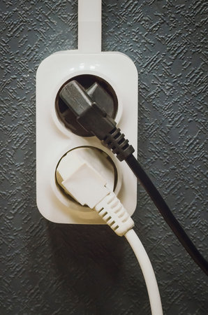 Electric white and black plugs and a white plastic plug on the wall.
