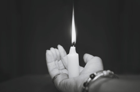 A glowing candle in the hands of a woman. Black and white photography.