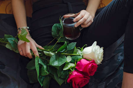 A bouquet of red and white roses, a glass with hot tea in the hands of a young girl close-up.の写真素材