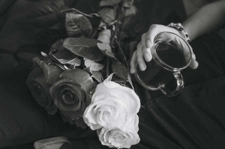 Close-up of a glass with tea in a female hand. A bouquet of roses, beautiful decoration. Black and white photography.の写真素材