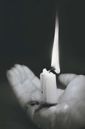 Burning out candle with melting wax on a woman's palm. Black and white vertical photography.の写真素材