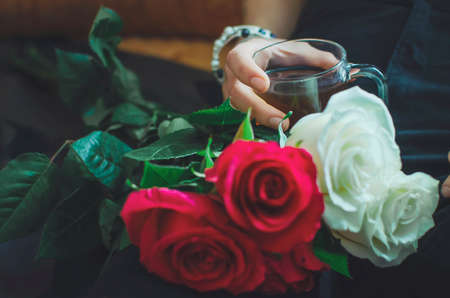 Close-up of hands holding a glass with tea and a bouquet of roses. Lifestyle concept.の写真素材