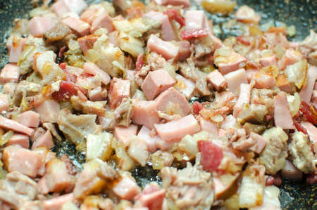 Different types of sausages and meat in a pan. Frying ingredients for making a hodgepodge. Close-up.の写真素材