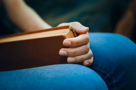 A girl in blue jeans holds a large book in her hands, close-up.の写真素材