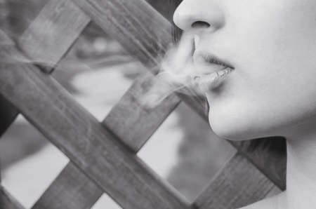 The girl smokes an electronic cigarette, exhaling smoke. Close-up, Black and white photography.の写真素材