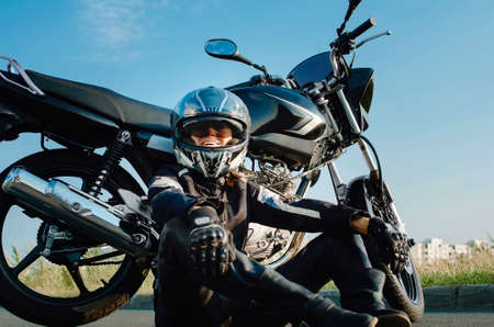 A middle-aged woman sits near her motorcycle and smiles. The concept of an active lifestyle at any age.の写真素材