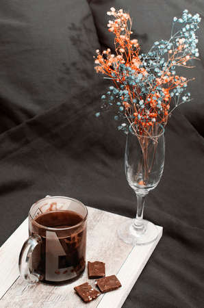 Flowers and coffee with chocolate in bed at home. Cozy home interior, black linens. Vertical photography.の写真素材