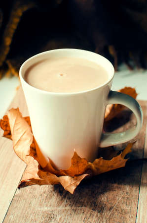 Delicious hot coffee with milk on a wooden table with autumn dry leaves. Vertical photography. Beautiful autumn background.の写真素材