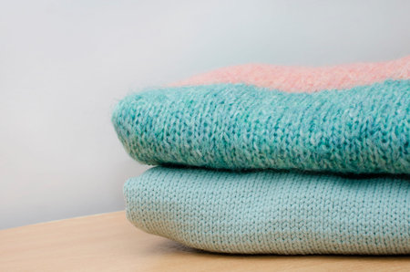 Two folded blue knitted sweaters on a neutral background.