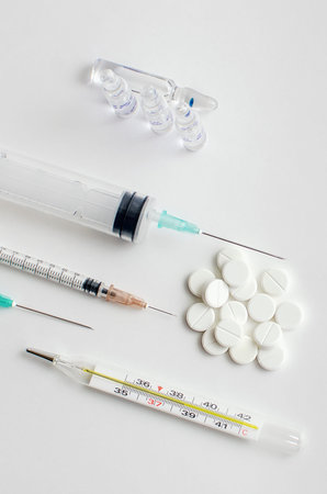 Pills, thermometer, syringe on a White background, top view. First aid, care during illness....