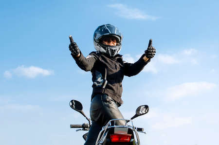 Woman on motorcycle against blue skywith thumbs up because something good has happenedの写真素材