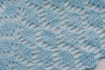 Fragment of a knitted woolen scarf close-up. Nice blue knitting pattern, all the loops are visible.
