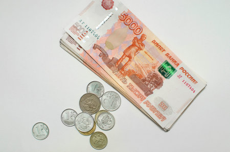 Iron coins next to a stack of five thousandth bills. Russian money on a white background, top view.