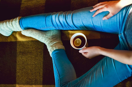 A glass of tea with lemon close-up in the hands of a girl. Close-up of legs dressed in blue jeans...