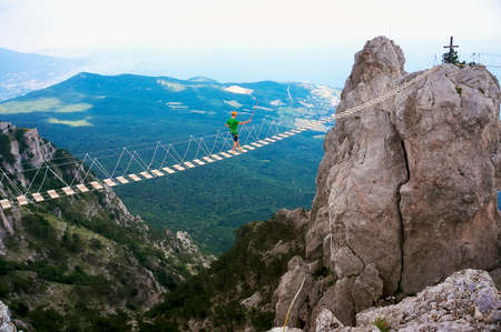 Amazing view of the high rope bridge with traveler above abyss against the Black Sea coast. Scenery of Crimea in summer.の写真素材
