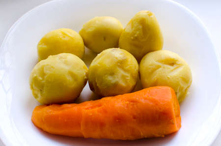 Boiled peeled potatoes and carrots on a white plate.の写真素材