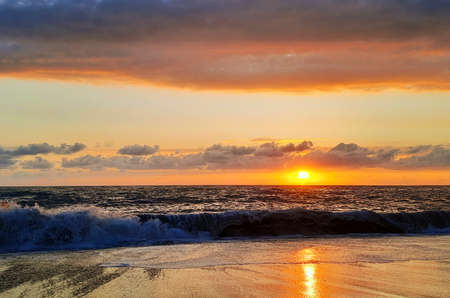 Reflections of setting sun over coast at sunset.の写真素材