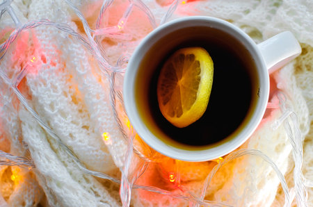 Hot lemon tea on the background of knitted fabric with a festive garland of lights. Close-up,...