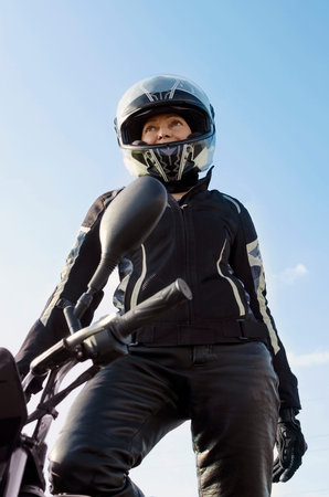A woman in a motorcycle helmet and a protective suit against the blue sky. vertical photography.