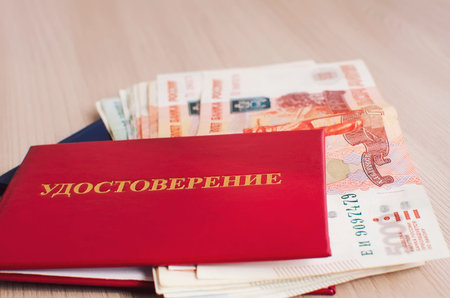 A Russian identity card in a red cover and a bundle of Russian money lie on the table, close-up. The...