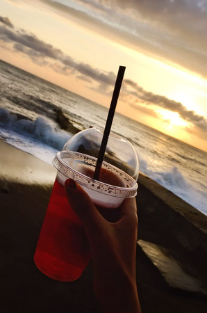juice in a plastic glass in a hand against the background of the setting sun.