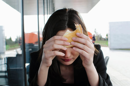 A girl at a table in a cafe eats a hamburger, close-up.