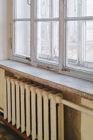 Old wooden window with a cast iron radiator. Vertical photography.