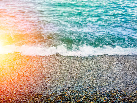 Waves breaking on the multicolored sea pebbles Black Sea coast. Beautiful natural background. Beautiful sunset sun.の写真素材
