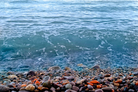 Blue waves roll onto the multicolored sea pebbles Black Sea coast. Beautiful natural background.の写真素材