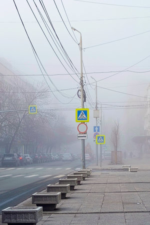 City street in thick fog. The road with cars, the sidewalk and the traffic light are hidden in the fog.の写真素材