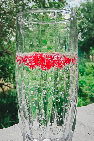 Red current berries in a glass of sparkling mineral water on a natural background. Non-alcoholic refreshing healthy drink with vitamins.の写真素材