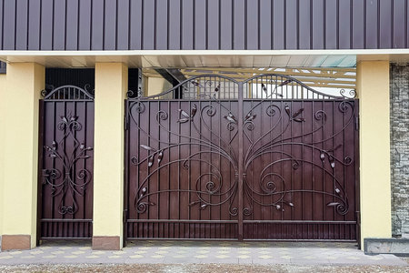 Modern brown metal gate with wrought iron patterned grille and concrete posts.