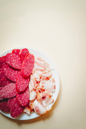 Sliced pieces of smoked sausage and bacon on a neutral background. Vertical photo.の写真素材