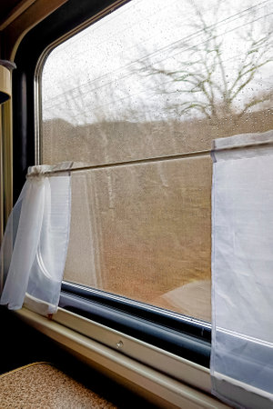 train window in a moving train. Large window with landscape, daytime, autumn, no people. Close-up, vertical photo.の写真素材