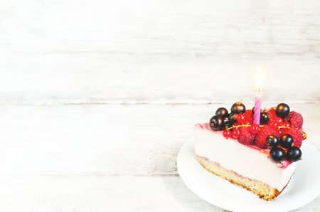 birthday cheesecake with candle, raspberries, red and black currants on a white wood backgroundの写真素材