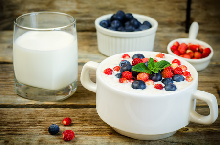oatmeal with blueberries and strawberries in the white bowl on a dark wood background.の写真素材
