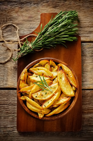 potatoes baked with rosemary on a dark wood background. toning. selective focus on rosemary on potatoの写真素材