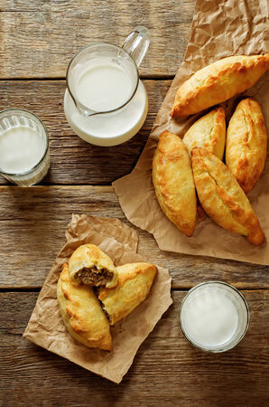 pasties stuffed meat and glass of milk on a dark wood background. tinting. selective focus on the meatの写真素材