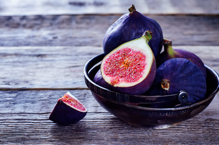 figs on a dark wood background. tinting. selective focus on the front figs slice in the bowlの写真素材